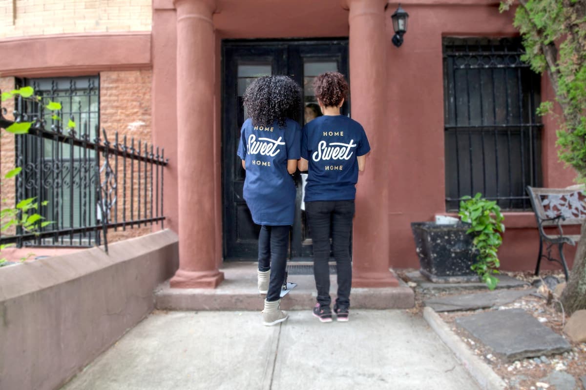Two cleaners in Home Sweet Home uniform tees waiting at a front door, photographed from behind