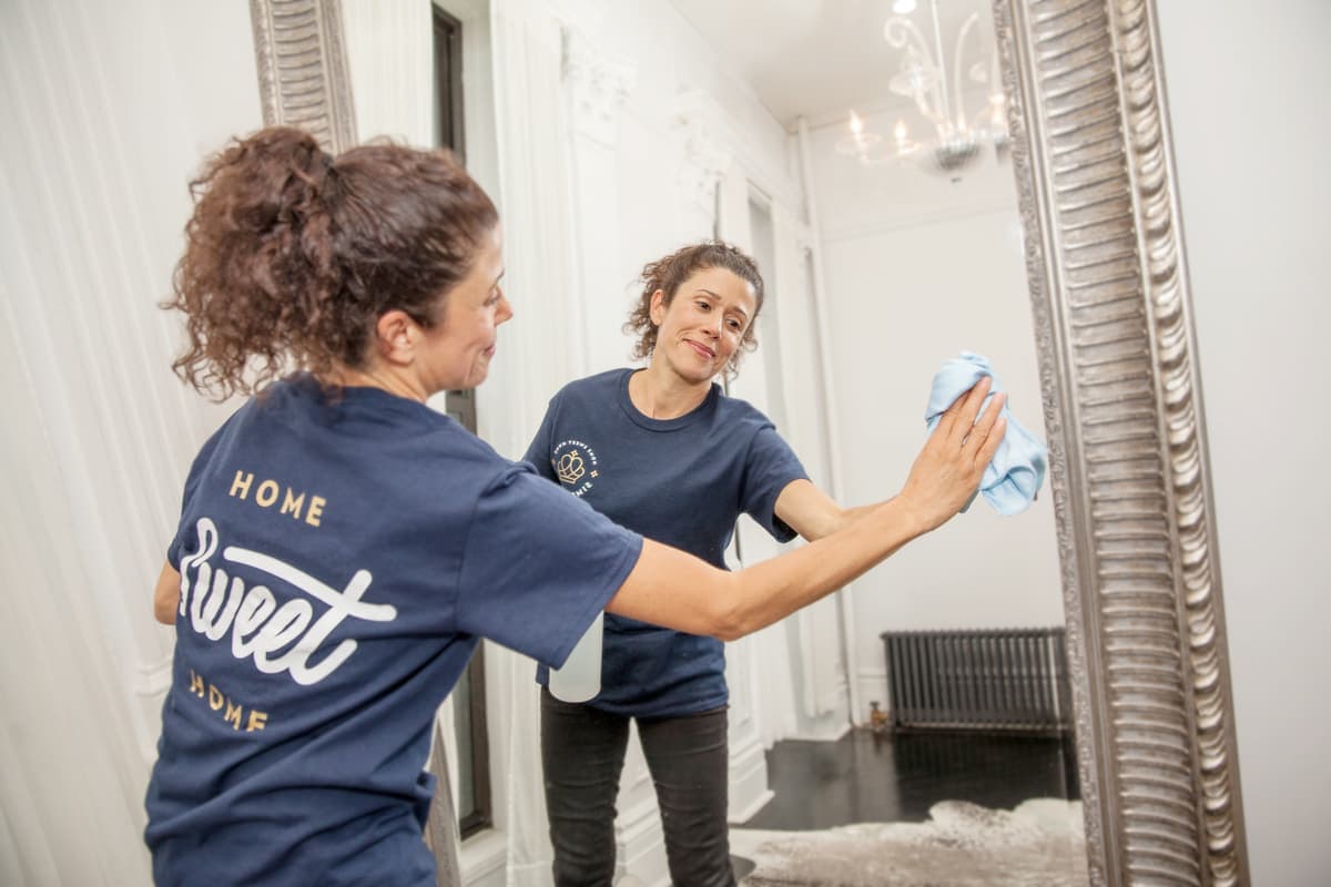 A cleaner polishing a large framed mirror with a microfibre cloth