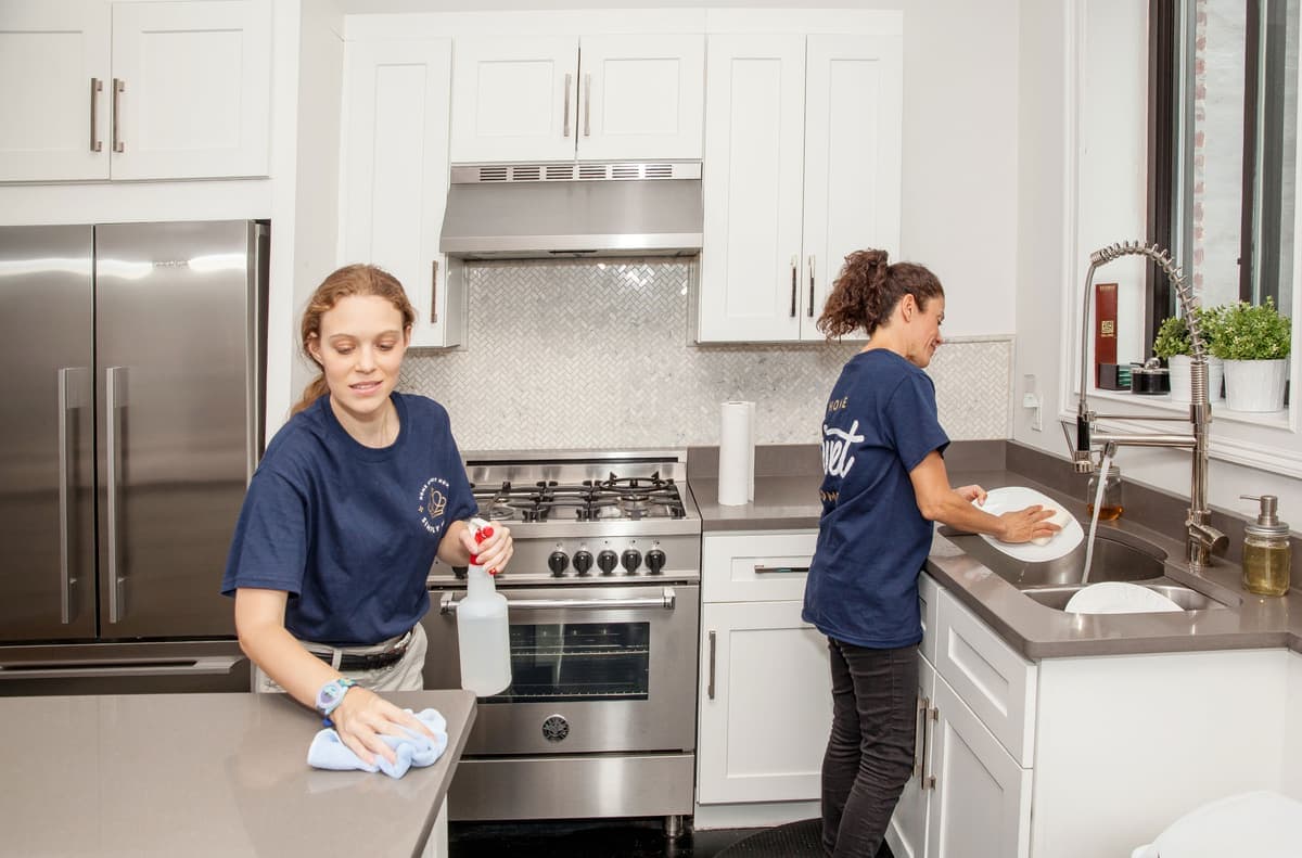 Two cleaners working a kitchen, one wiping a benchtop and one at the sink