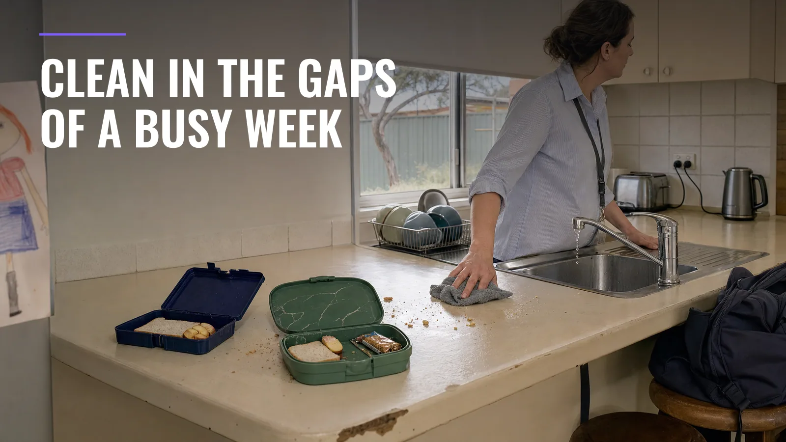 A parent wipes crumbs from a kitchen bench beside two open lunchboxes at breakfast, a school bag slung on a stool behind.
