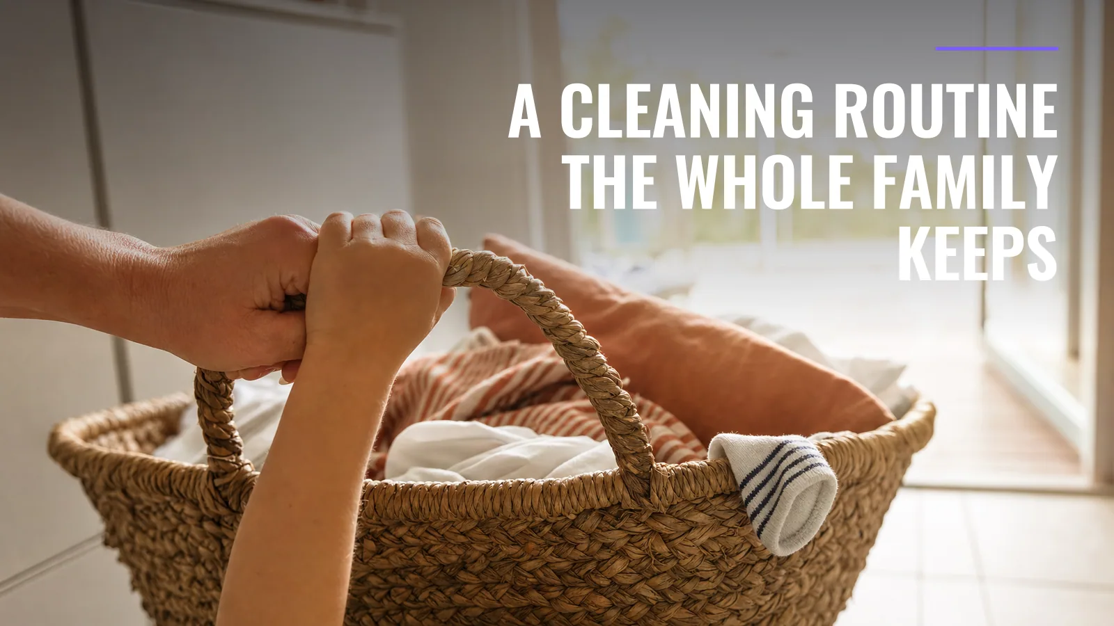 A child's hand and an adult's hand share the handle of a woven laundry basket of clean washing, lit from behind by a bright glass door to a deck.