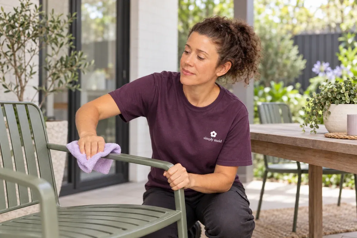 A cleaner wipes the arm of an outdoor chair under a patio.