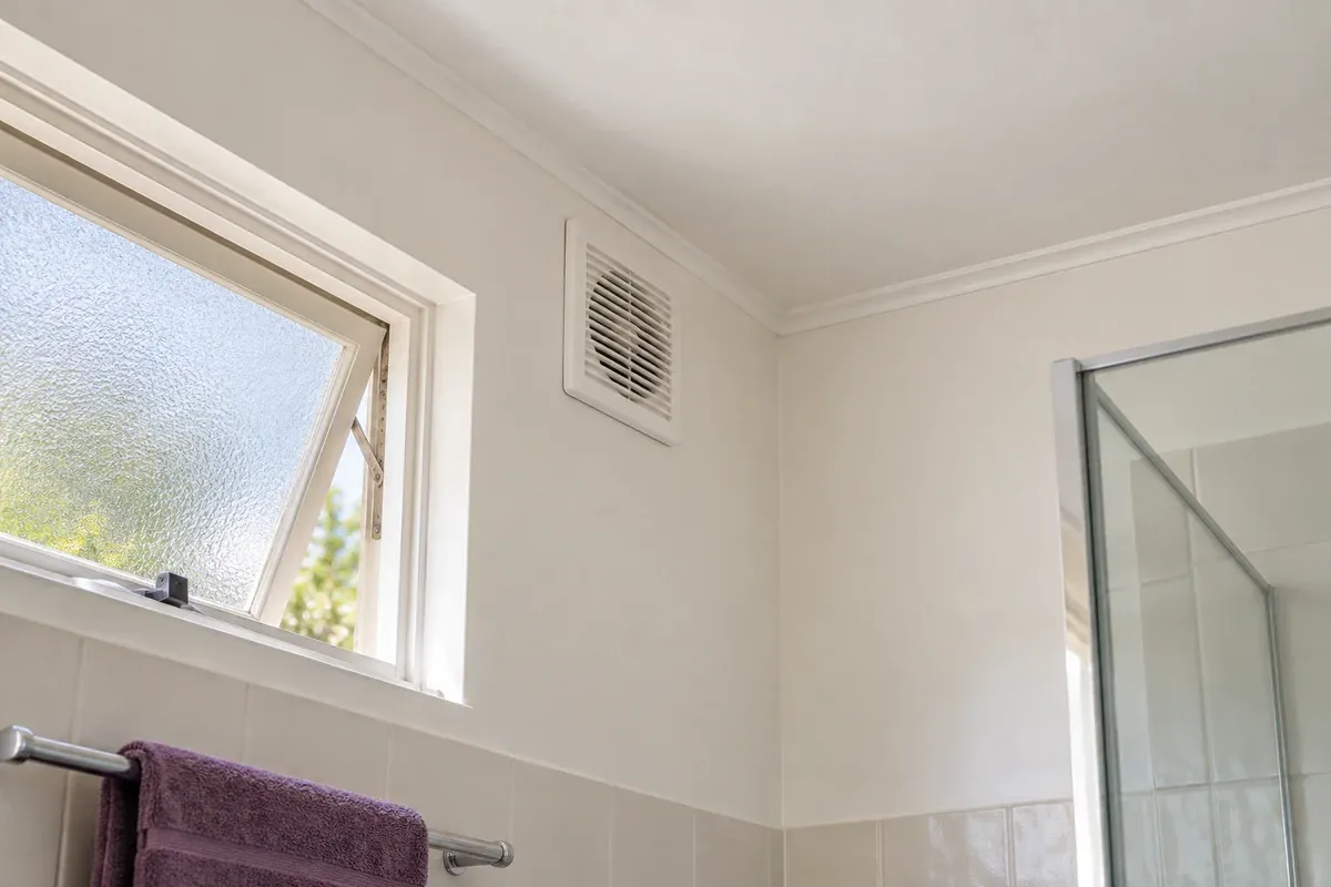 The wall and ceiling corner of a bathroom beside an open window and exhaust fan.