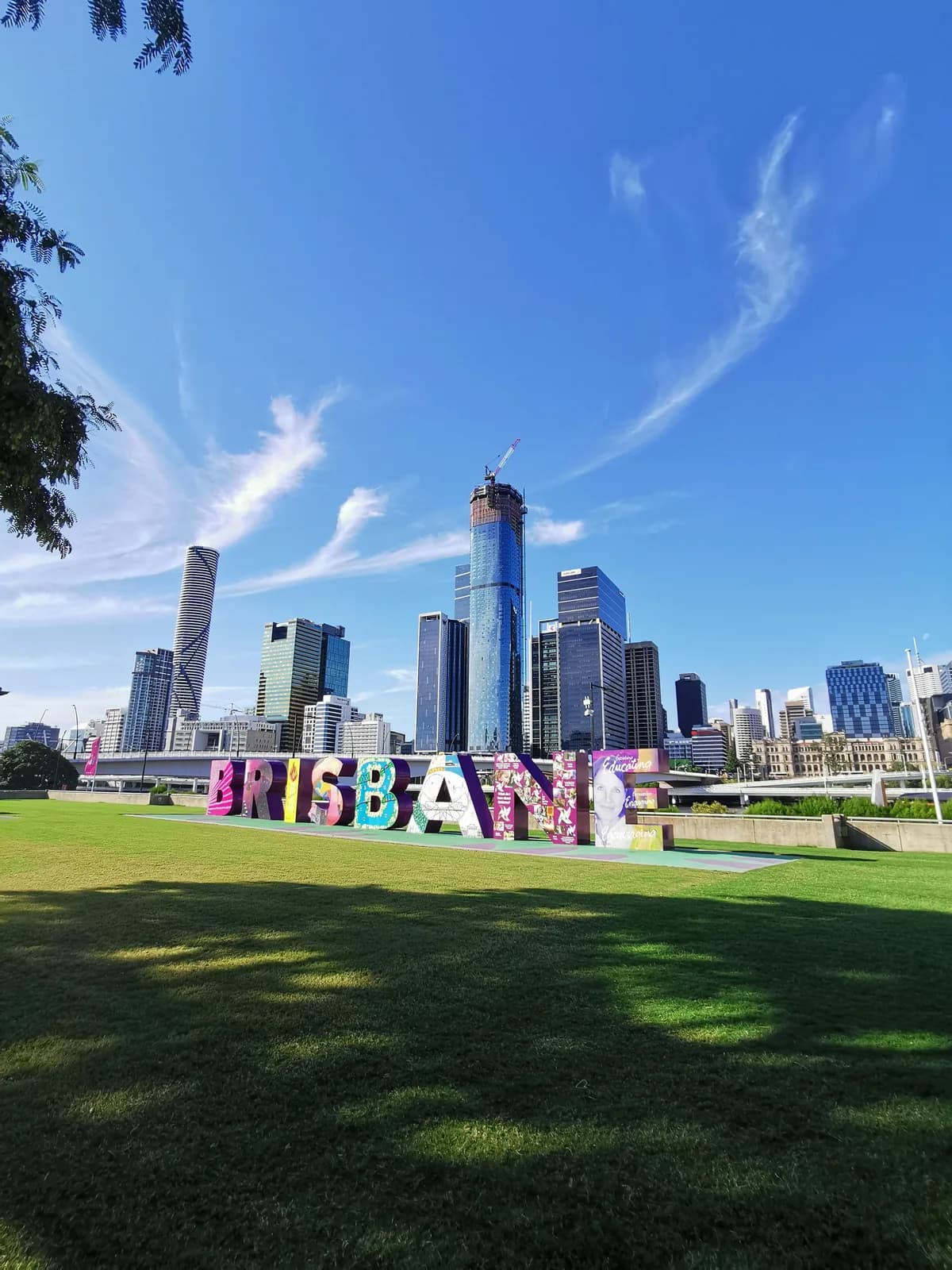 Brisbane's South Bank lawn and colourful Brisbane sign, with city buildings behind.