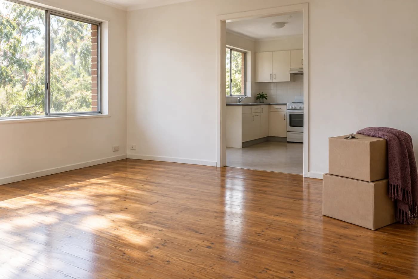 Packed moving boxes and keys in an empty Australian rental, with timber floors and an open kitchen doorway.